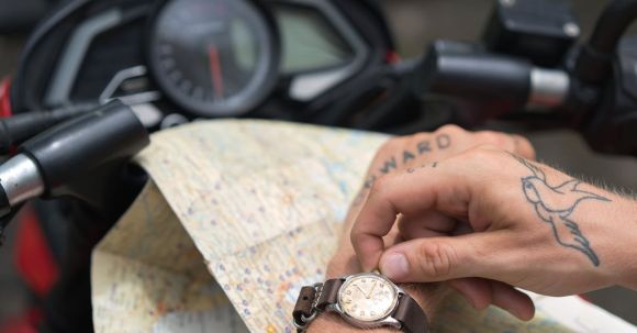 Motorcycle License Time - Crop tattooed man setting up watch against map and motorbike