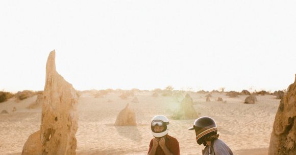 Motorcycle License Timing - Anonymous tourists in protective helmets talking while sitting on bikes on sandy land during summer trip