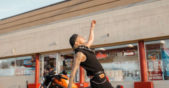 Motorcycle License Tips. - Man Standing on Tip Toes with his Arms Raised next to a Motorcycle