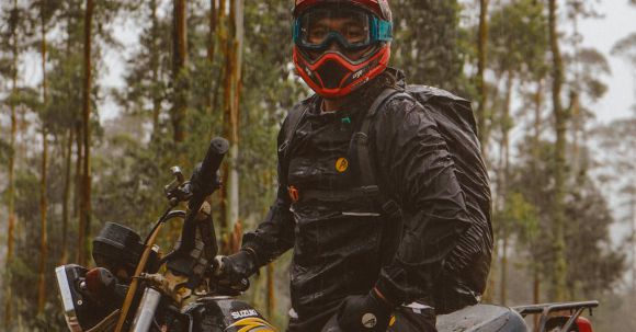 Moto Riding - Side view of male biker in protective helmet with backpack sitting on motorcycle in woods