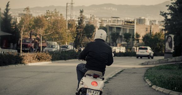 Moto Riding - Back view of anonymous man in helmet riding motorcycle on asphalt road near cars in city outskirts