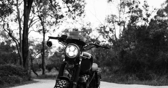 Moto Riding - Black and white of motorcycle parked on sandy ground near trees and grass