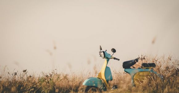 Motorcycle Photography - Vintage blue and yellow motorcycle parked on lawn amidst flowers and grass in countryside on clear day