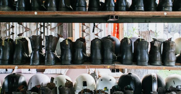 Choose Right Helmet - Abundance of leather old fashioned boots placed on wooden shelves near plastic protective helmets for rent on street in city