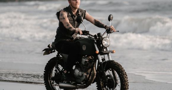 Moto Riding - Tattooed motorcyclist riding bike along ocean coast in evening