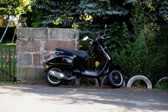 Moto Riding - a black scooter parked next to a brick wall