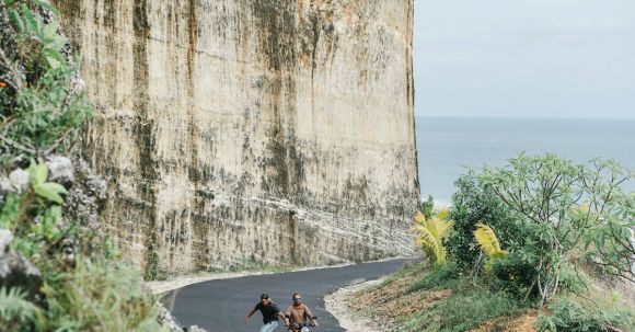 Cultural Motorcycle Experience - Full length unrecognizable male skater and biker riding on road together against mountain slope and horizon