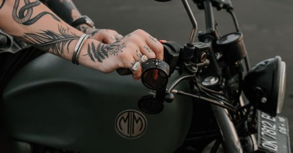 Motorcycle Registration: Essentials - Side view of crop faceless tattooed male rider in silver rings and metal wristband sitting on modern motorcycle with side mirrors and registration mark on sandy sea beach