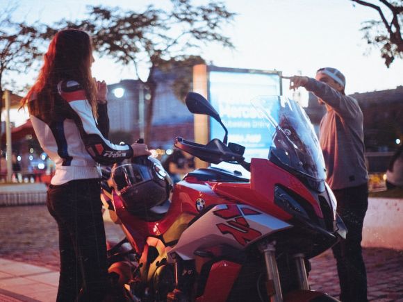 Moto Riding - two people standing next to a parked motorcycle