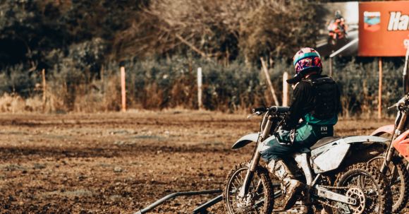 Off-road Safety Tips - Back view of anonymous person in helmet parking motorbike on dirty ground on sunny day in countryside