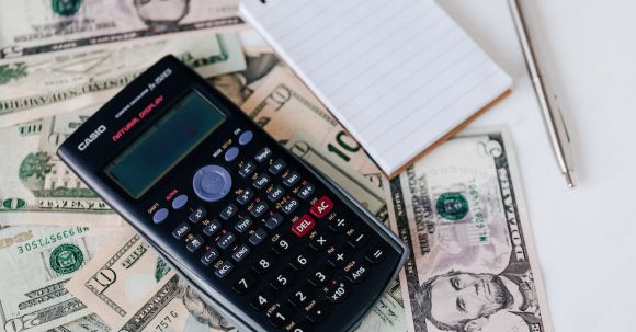 Insurance Bundling. - From above electronic calculator and notepad placed over United States dollar bills together with metallic pen for budget planning and calculation