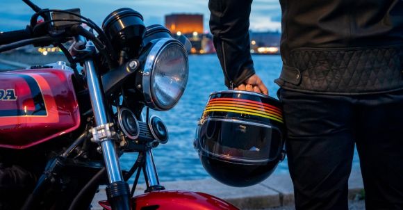 Motorcycle Helmet - man in black jacket and black pants standing beside black motorcycle during daytime