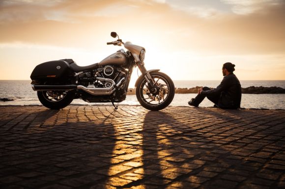 Motorcycle - man sitting on ground beside parked silver cruiser motorcycle