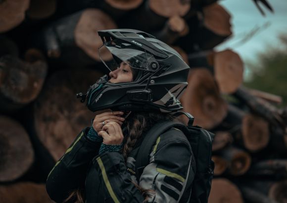 Moto Clothes - a woman wearing a helmet standing in front of a pile of logs
