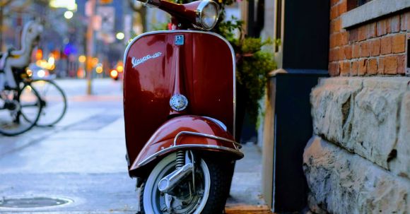 Motorcycle Safety: Brand. - Red Piaggio Vespa Motor Scooter Parked Beside Gray and Red Concrete Building