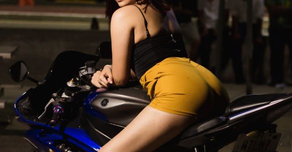 Top Motorcycles - Young Brunette Woman in Black Top and Yellow Shorts Sitting on a Motorcycle
